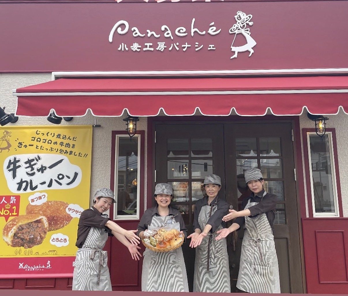 赤いひさしの店頭で、パンのかごを手に笑顔で迎えるパナシェのスタッフ4名